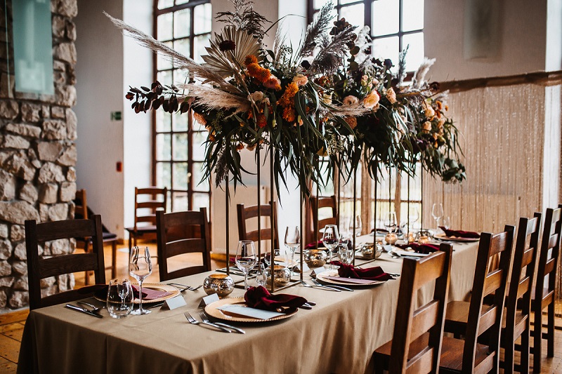 Garnitur dla Pana Młodego wysokie dekoracje na weselu, standy na stole weselnym, prostokątne stoły na weselu,  Pomysł na ślub i wesele jesienią w  modnych kolorach roku 2021 - rdzawe pomarańcze, klasyczne borda i ciemne burgundy