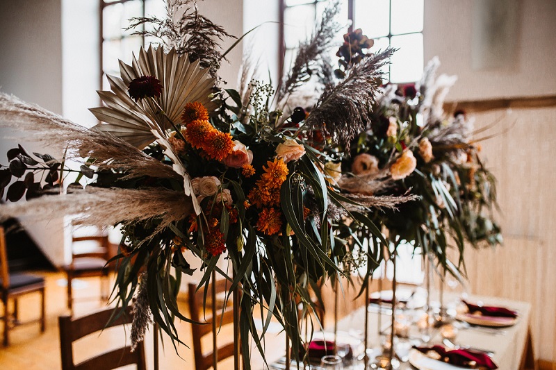 wysokie dekoracje na weselu, standy na stole weselnym, prostokątne stoły na weselu,  Pomysł na ślub i wesele jesienią w  modnych kolorach roku 2021 - rdzawe pomarańcze, klasyczne borda i ciemne burgundy