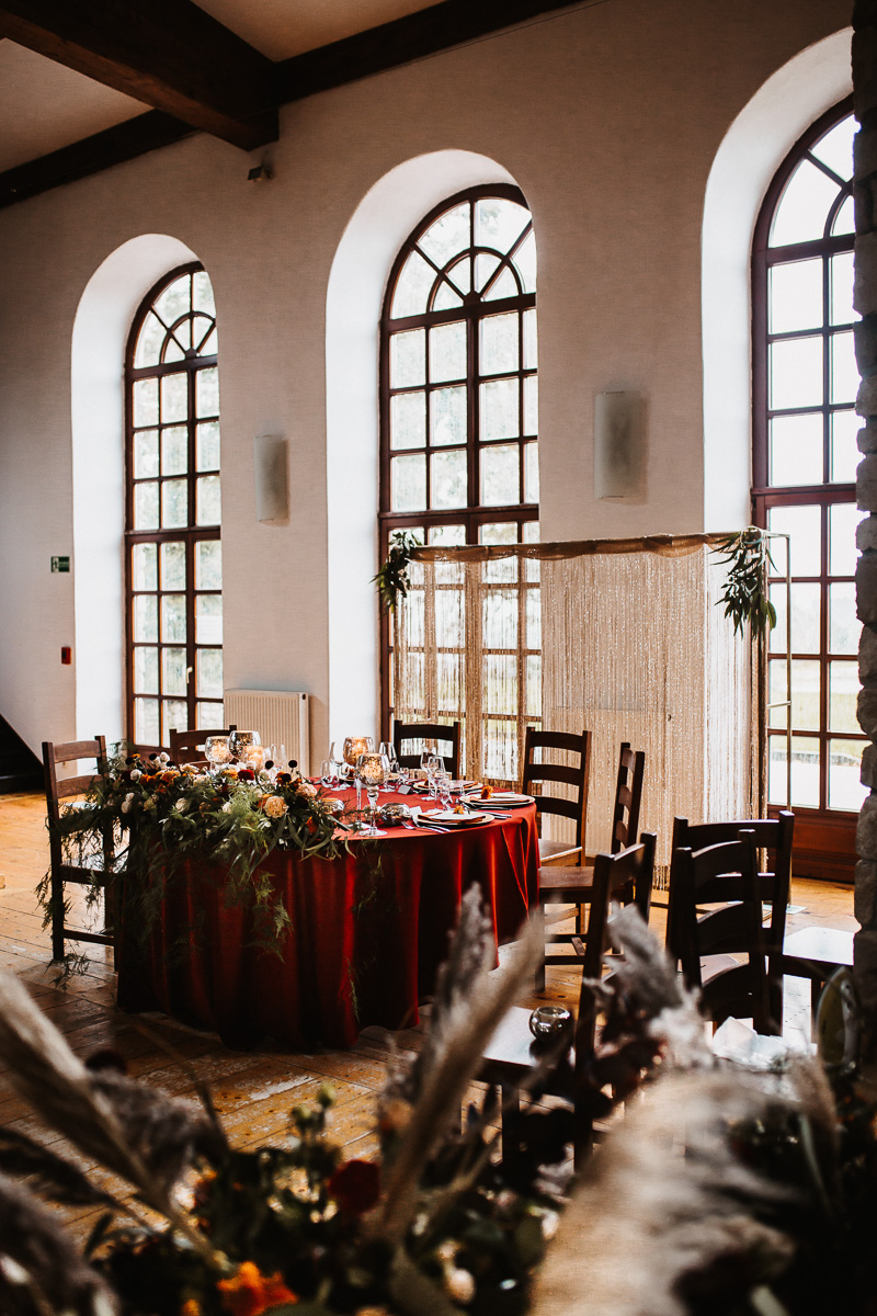 stół pary młodej wysokie dekoracje na weselu, standy na stole weselnym, prostokątne stoły na weselu,  Pomysł na ślub i wesele jesienią w  modnych kolorach roku 2021 - rdzawe pomarańcze, klasyczne borda i ciemne burgundy